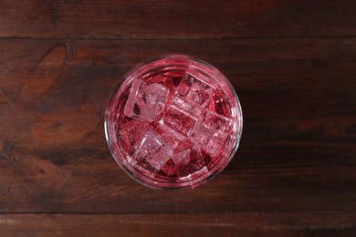 Photo of Sweet soda water with ice cubes in glass on wooden table, top view