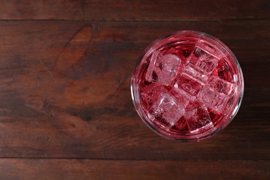 Photo of Sweet soda water with ice cubes in glass on wooden table, top view. Space for text