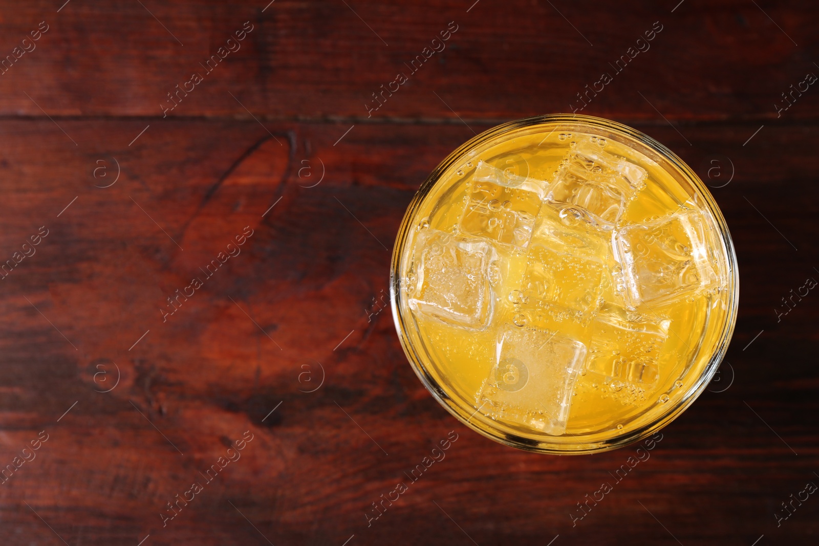 Photo of Sweet soda water with ice cubes in glass on wooden table, top view. Space for text