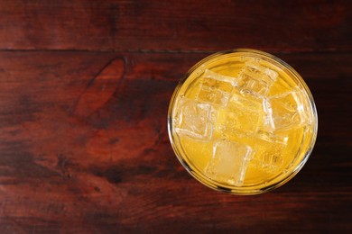 Photo of Sweet soda water with ice cubes in glass on wooden table, top view. Space for text