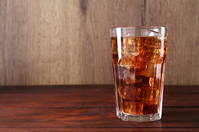 Photo of Sweet soda water with ice cubes in glass on wooden table, space for text