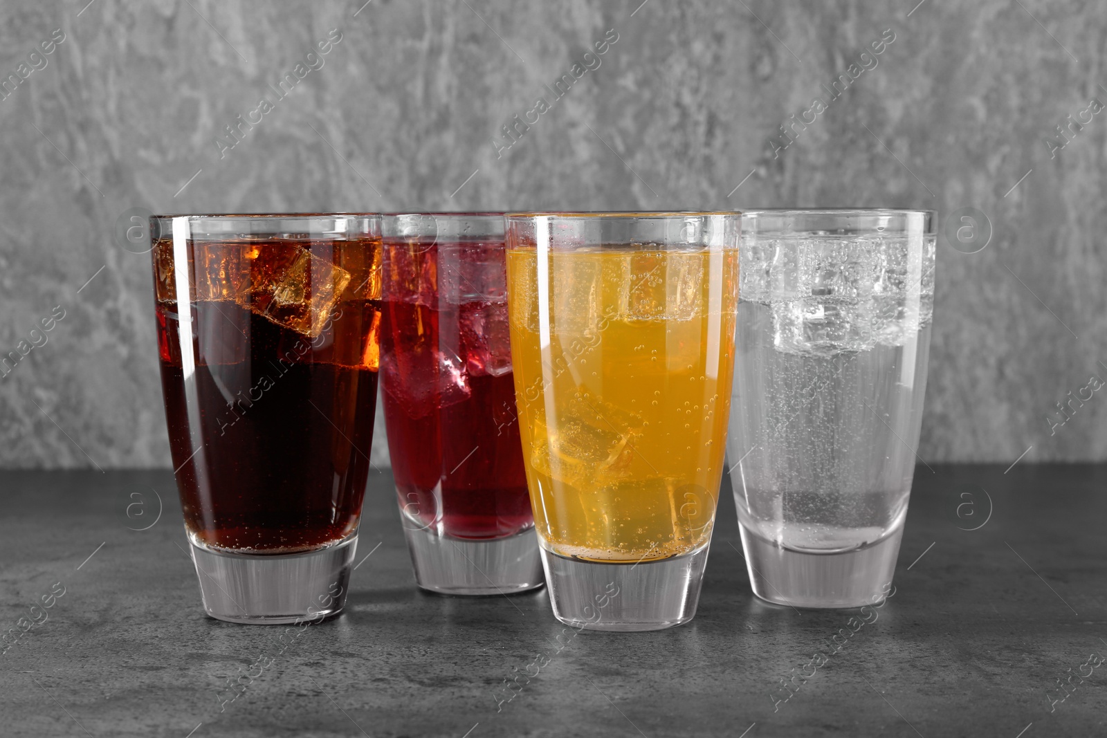 Photo of Sweet soda water of different flavors with ice cubes in glasses on grey table