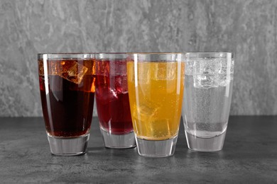 Photo of Sweet soda water of different flavors with ice cubes in glasses on grey table