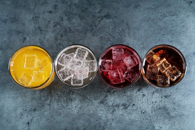 Photo of Sweet soda water of different flavors with ice cubes in glasses on grey table, flat lay