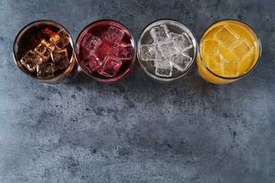 Photo of Refreshing soda water of different flavors with ice cubes in glasses on grey table, flat lay. Space for text