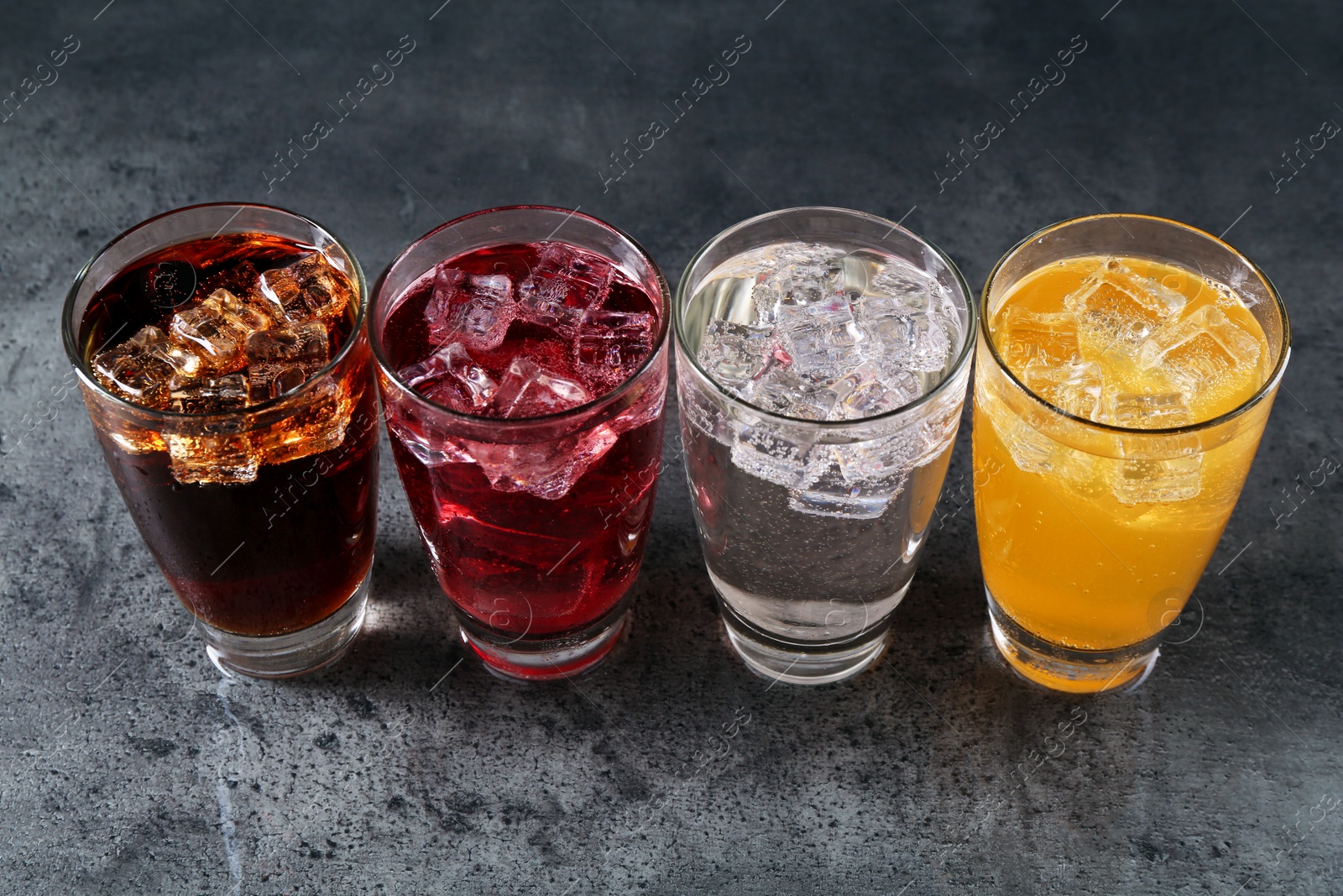 Photo of Sweet soda water of different flavors with ice cubes in glasses on grey table