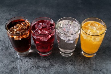 Photo of Sweet soda water of different flavors with ice cubes in glasses on grey table