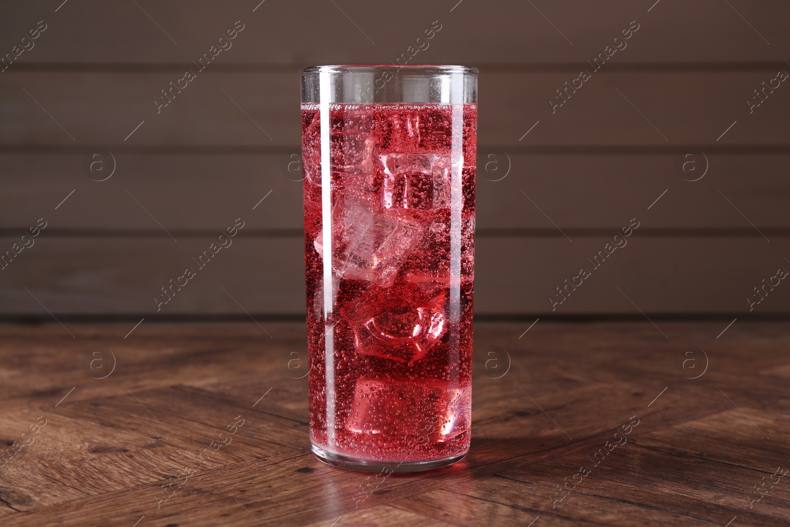 Photo of Sweet soda water with ice cubes in glass on wooden table