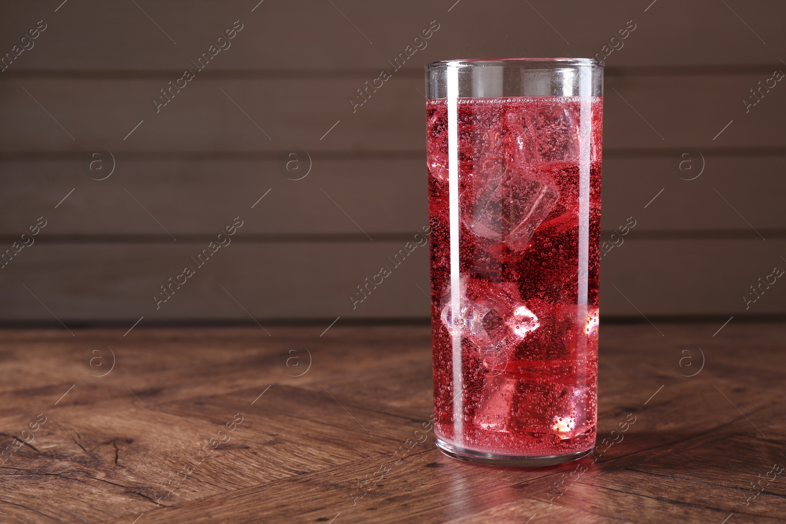 Photo of Sweet soda water with ice cubes in glass on wooden table, space for text