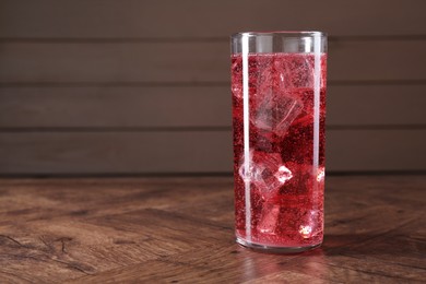 Photo of Sweet soda water with ice cubes in glass on wooden table, space for text