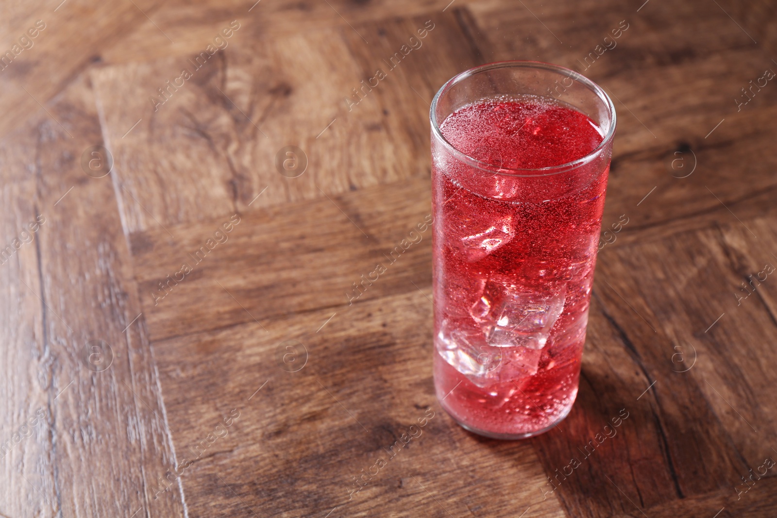 Photo of Sweet soda water with ice cubes in glass on wooden table, space for text