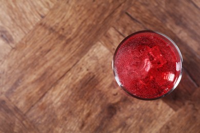 Photo of Sweet soda water with ice cubes in glass on wooden table, top view. Space for text