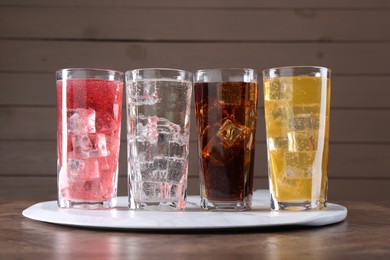 Photo of Refreshing soda water of different flavors with ice cubes in glasses on wooden table