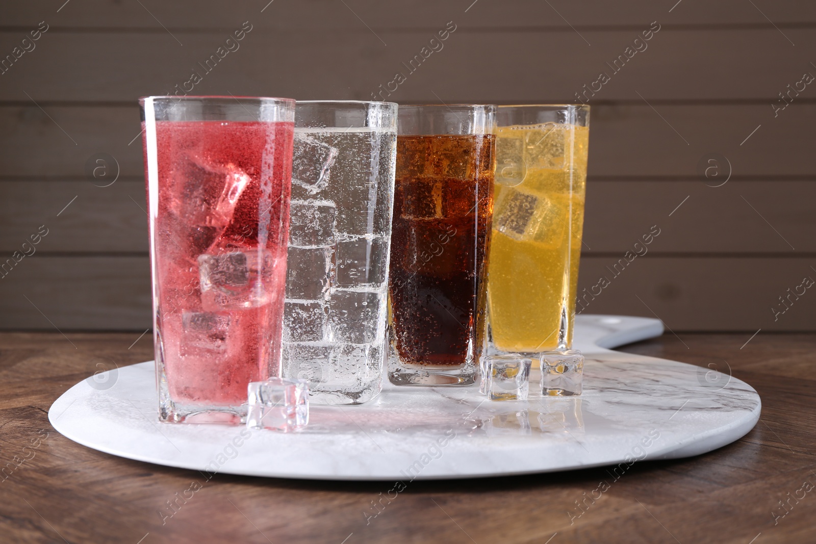 Photo of Sweet soda water of different flavors in glasses with ice cubes on wooden table