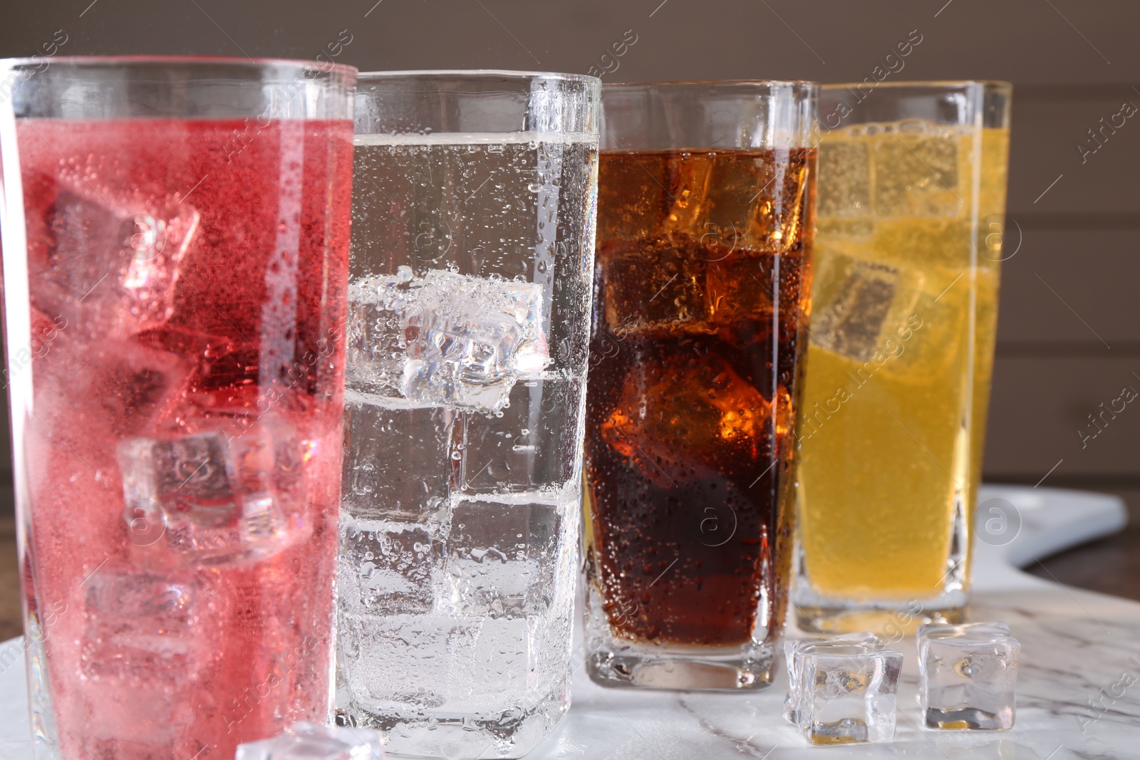 Photo of Refreshing soda water of different flavors with ice cubes in glasses on table, closeup