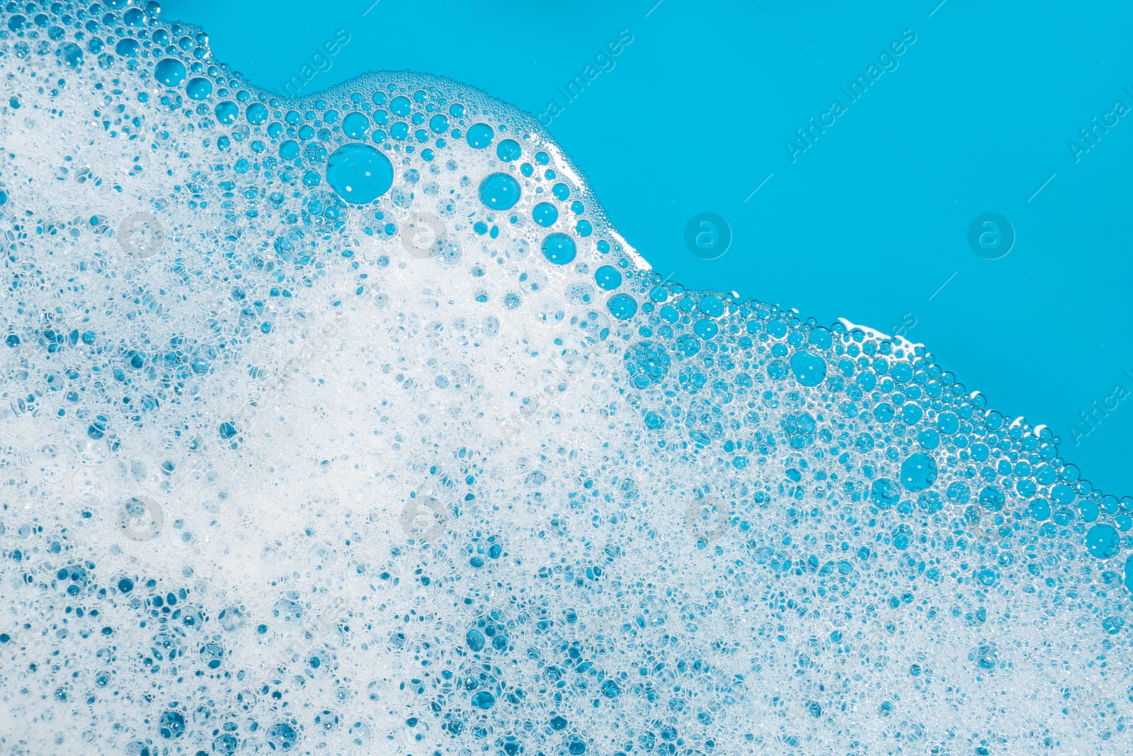 Photo of Detergent foam with bubbles on light blue background, top view