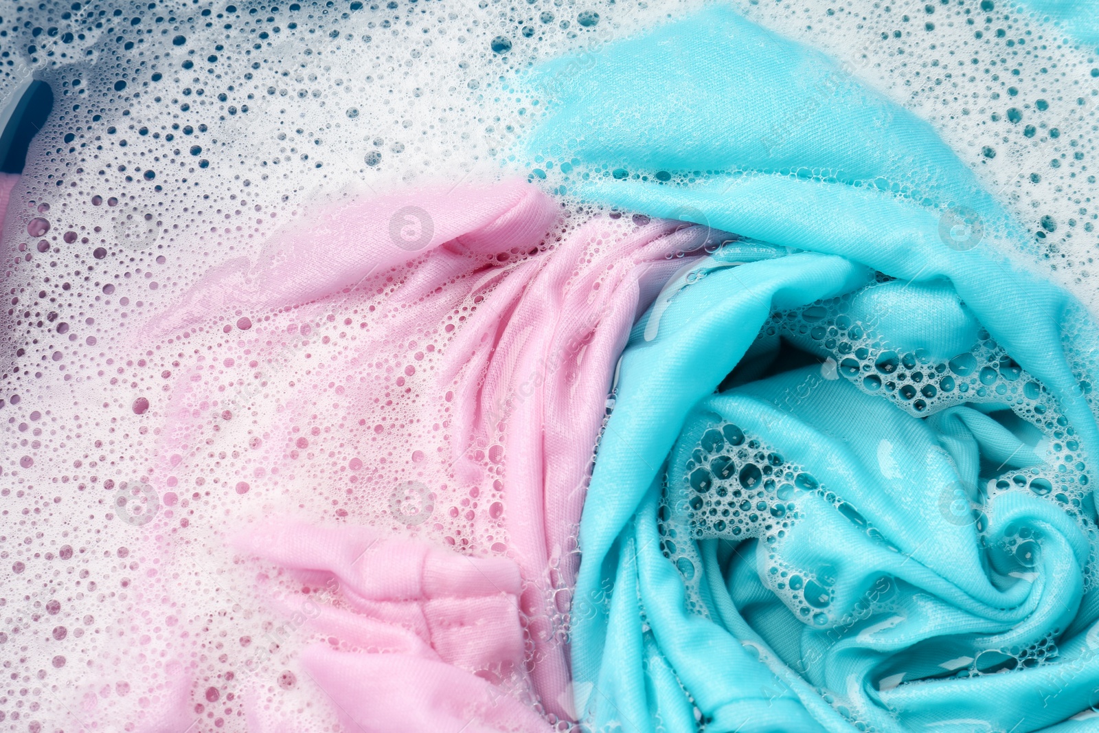 Photo of Colorful clothes soaked in water before washing, top view