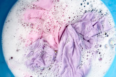 Photo of Colorful clothes soaked in water before washing, top view