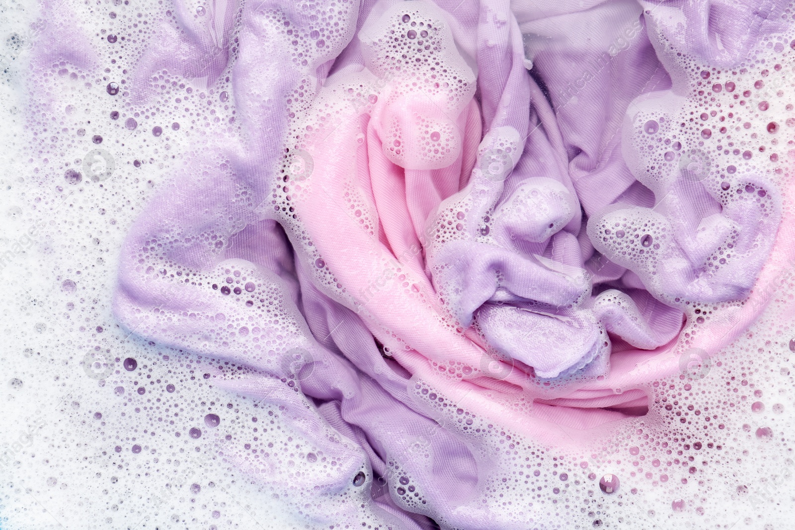 Photo of Colorful clothes soaked in water before washing, top view