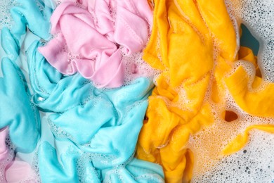 Photo of Colorful clothes soaked in water before washing, top view