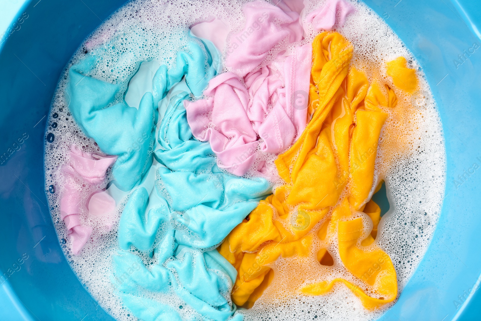 Photo of Colorful clothes soaked in water before washing, top view