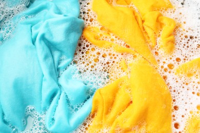 Photo of Colorful clothes soaked in water before washing, top view