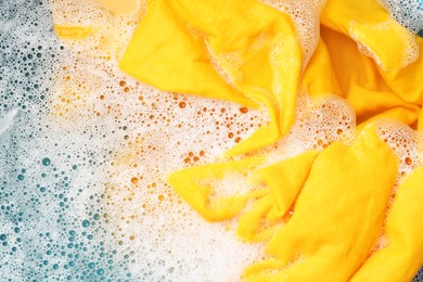 Photo of Yellow clothes soaked in water before washing, top view. Space for text