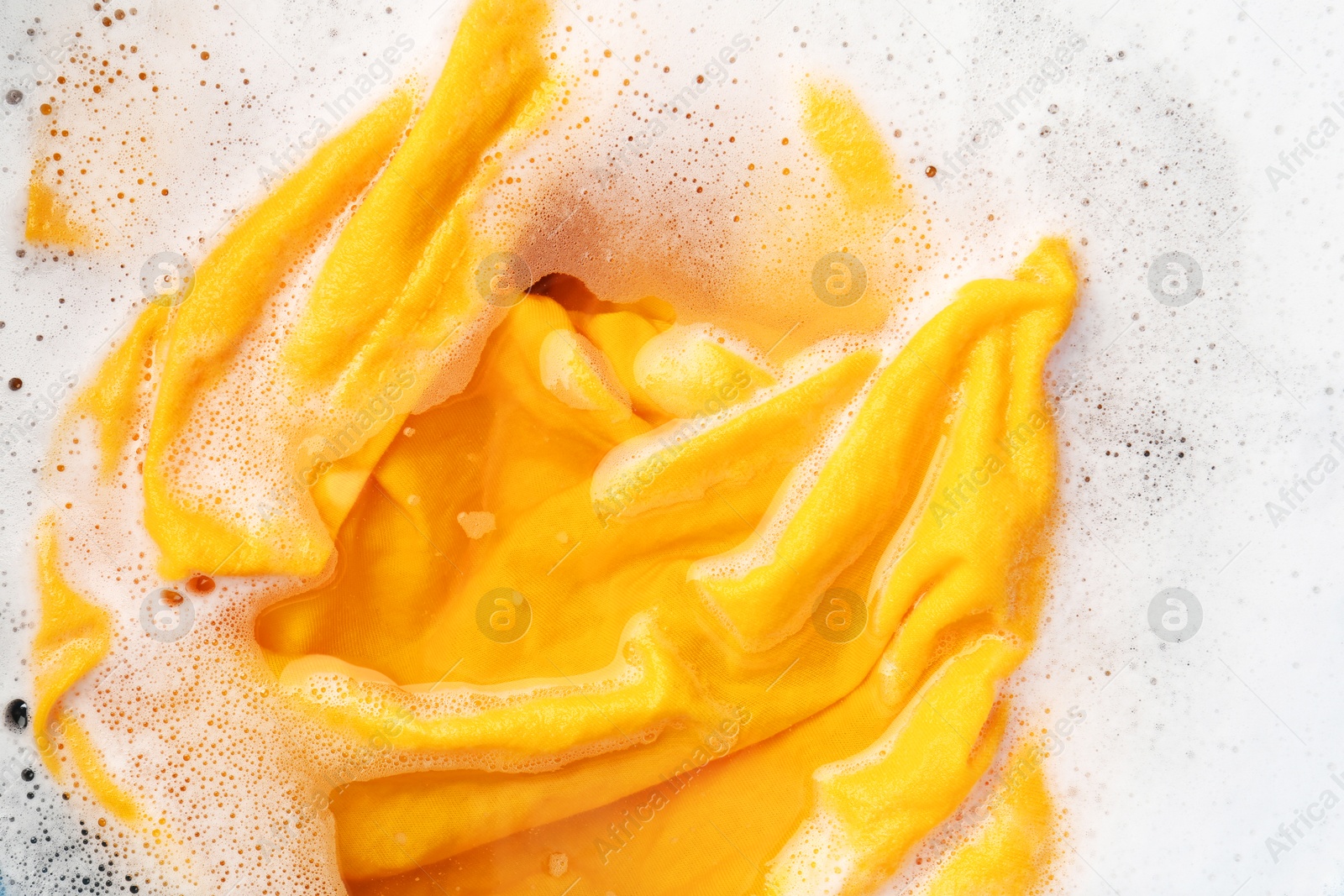 Photo of Yellow clothes soaked in water before washing, top view