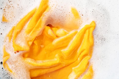 Photo of Yellow clothes soaked in water before washing, top view