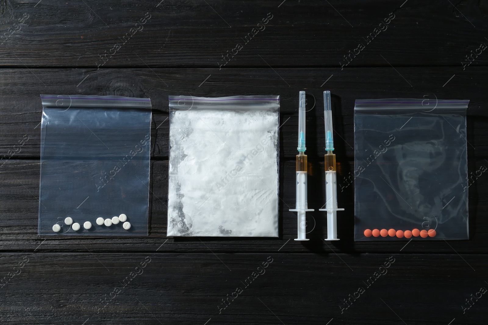 Photo of Drug addiction. Plastic bag with powder, syringes and pills on black wooden table, flat lay