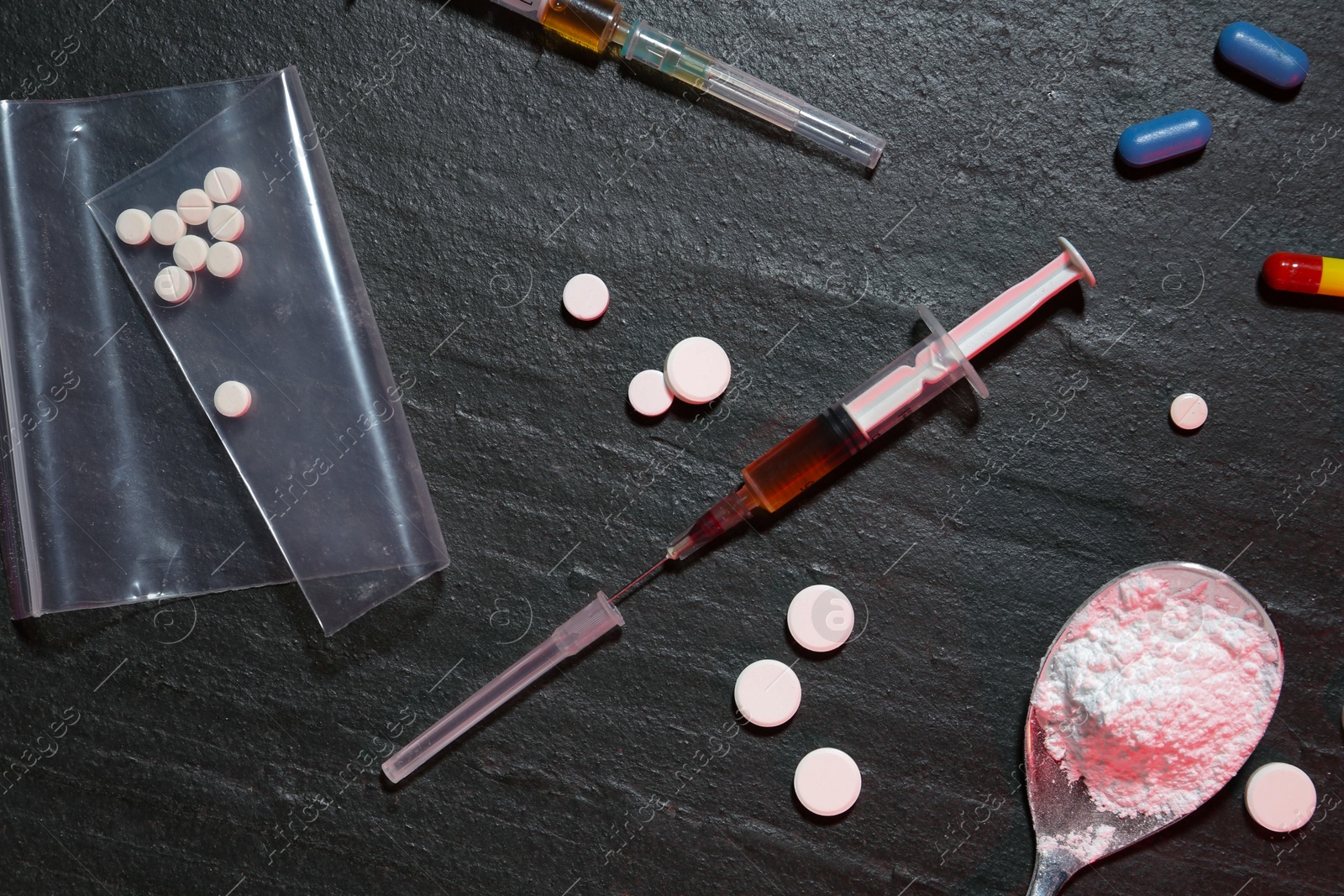 Photo of Drug addiction. Syringes, pills and spoon with powder on dark textured table, flat lay