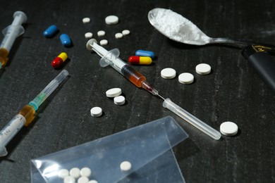 Photo of Drug addiction. Syringes, pills and spoon with powder on dark textured table, closeup