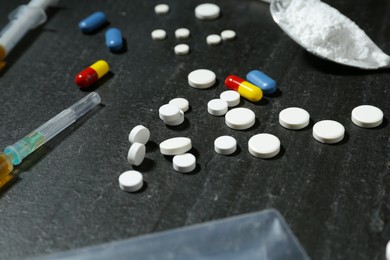 Photo of Drug addiction. Pills, syringes and spoon with powder on dark textured table, closeup