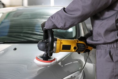 Photo of Man polishing car hood with orbital polisher indoors, closeup