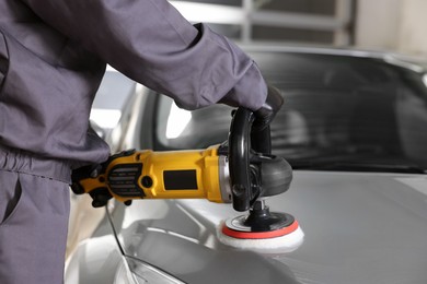 Photo of Man polishing car hood with orbital polisher indoors, closeup