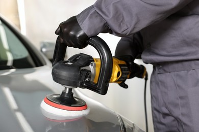 Photo of Man polishing car hood with orbital polisher indoors, closeup