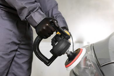 Photo of Man polishing car headlight with orbital polisher indoors, closeup