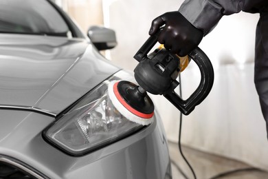 Photo of Man polishing car headlight with orbital polisher indoors, closeup