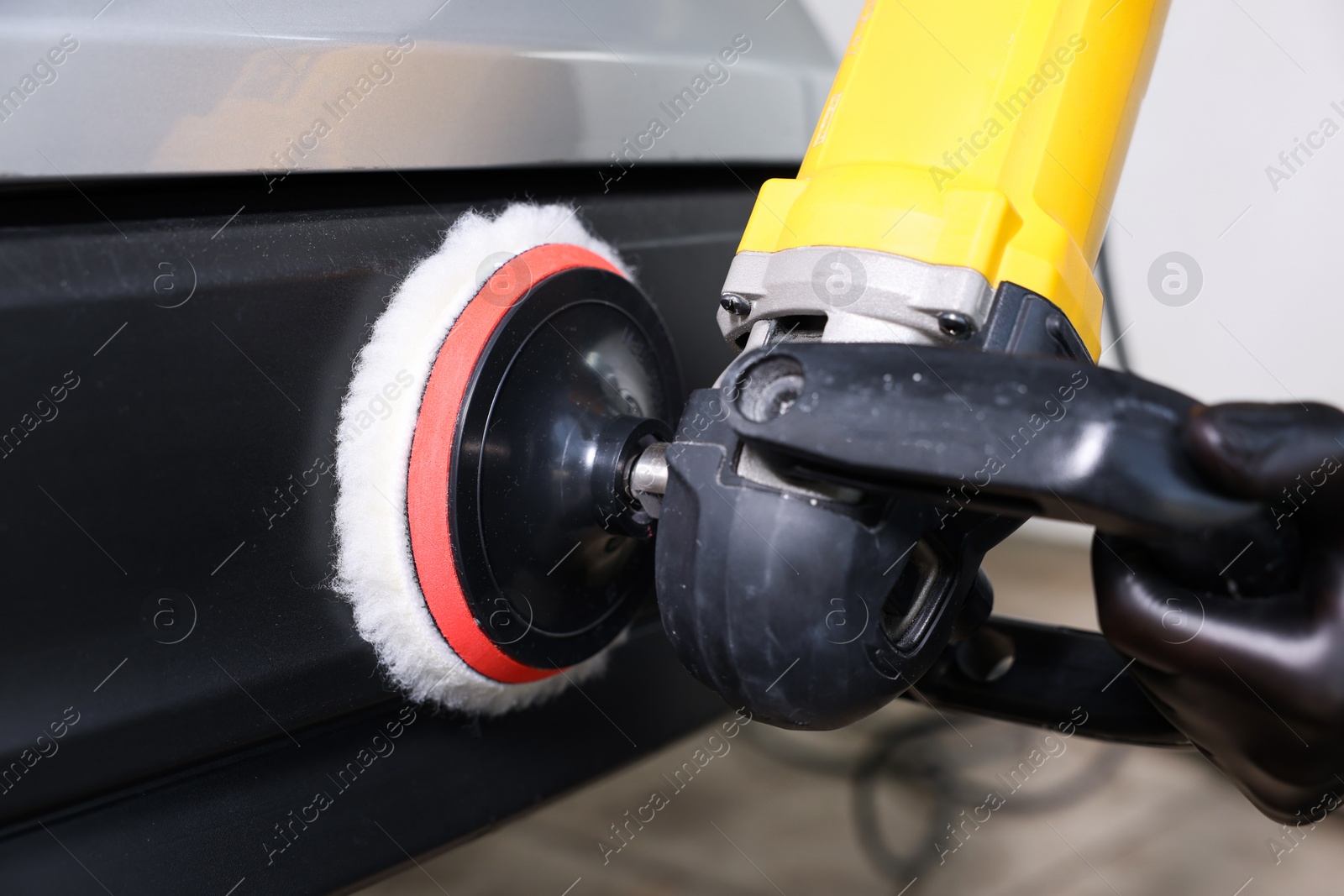 Photo of Man polishing car with orbital polisher indoors, closeup