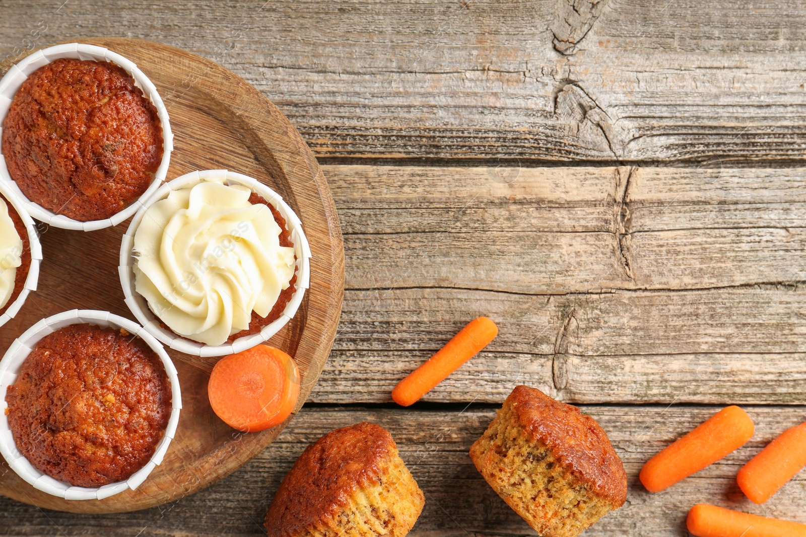 Photo of Delicious carrot muffins and fresh vegetables on wooden table, flat lay. Space for text