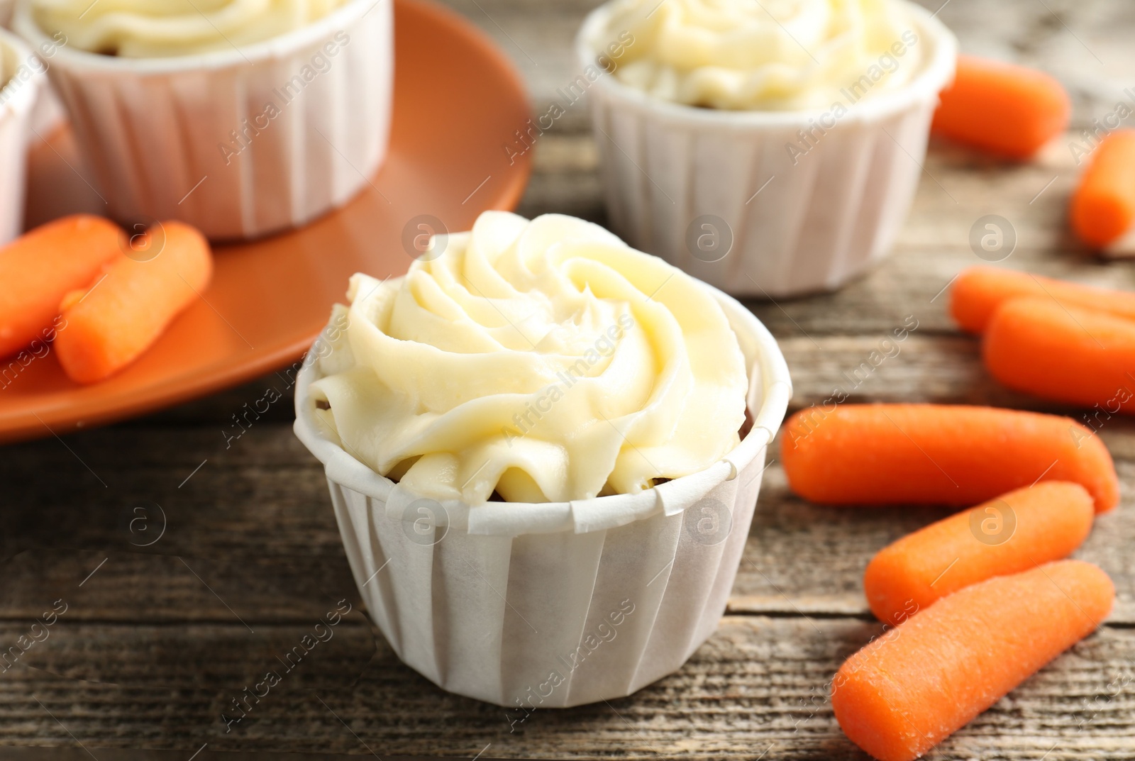 Photo of Delicious carrot muffins and fresh vegetables on wooden table, closeup