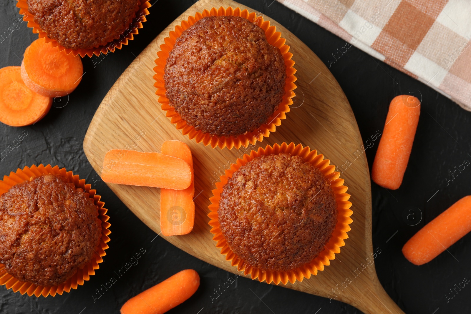 Photo of Tasty carrot muffins with fresh vegetables on black table, flat lay