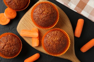 Photo of Tasty carrot muffins with fresh vegetables on black table, flat lay