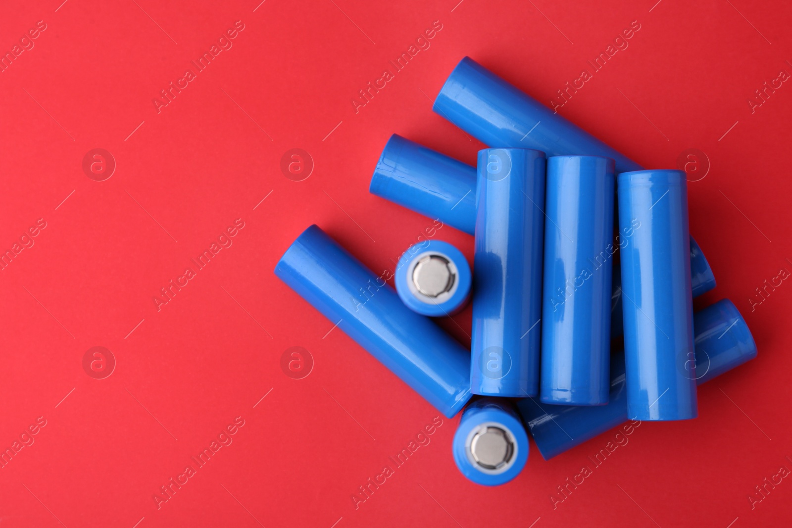 Photo of Many AA cell batteries on red background, top view. Space for text