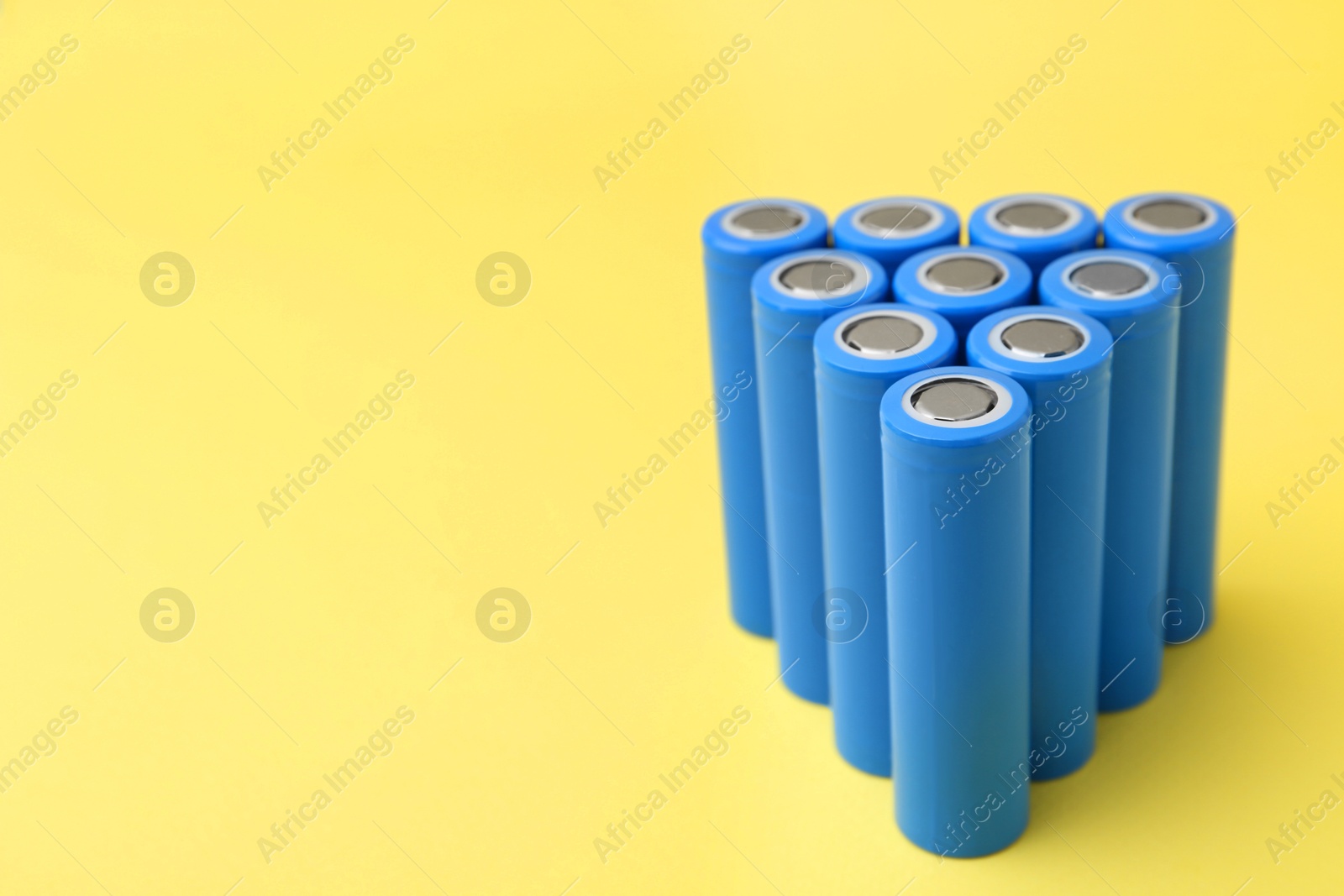 Photo of Many AA cell batteries on yellow background, closeup. Space for text