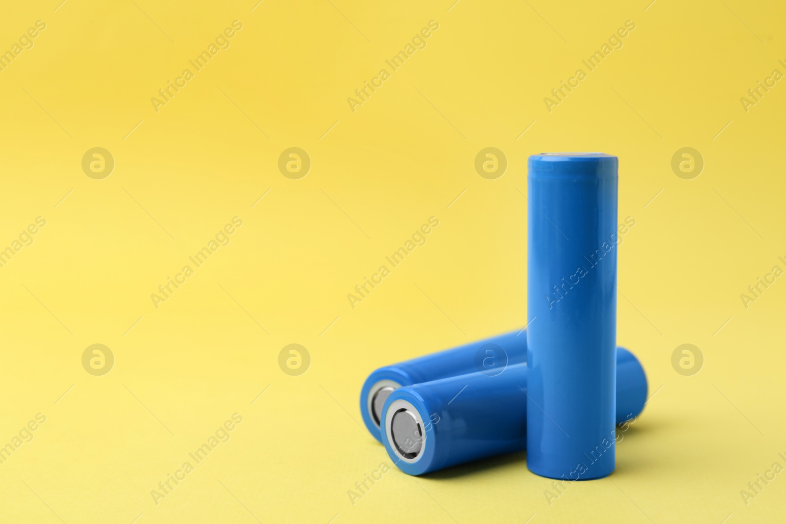 Photo of Three AA cell batteries on yellow background, closeup. Space for text