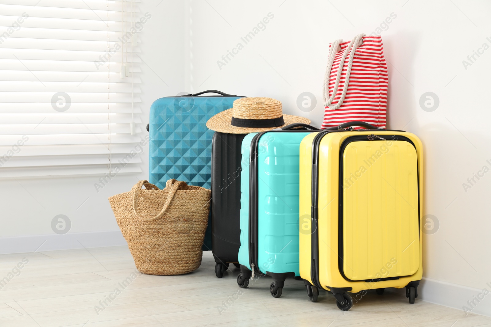 Photo of Colorful suitcases, beach bags and straw hat on floor near white wall