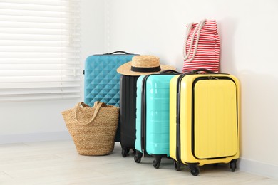 Photo of Colorful suitcases, beach bags and straw hat on floor near white wall