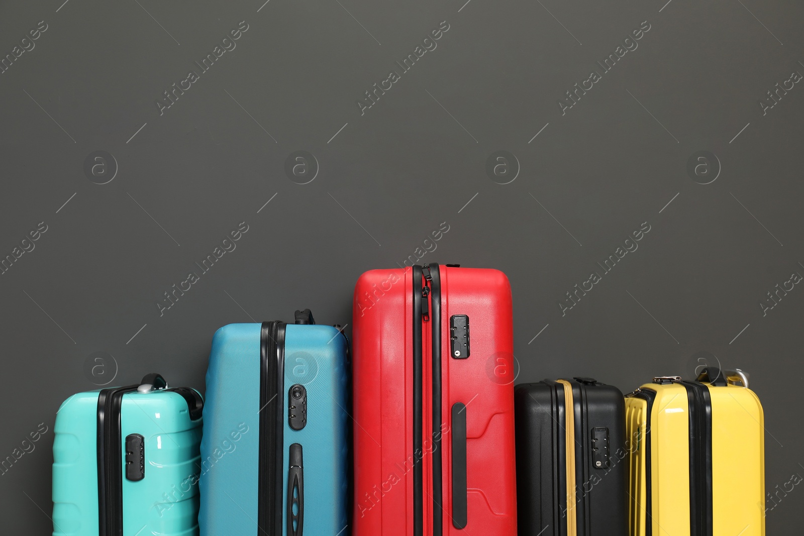 Photo of Colorful suitcases near black wall, space for text