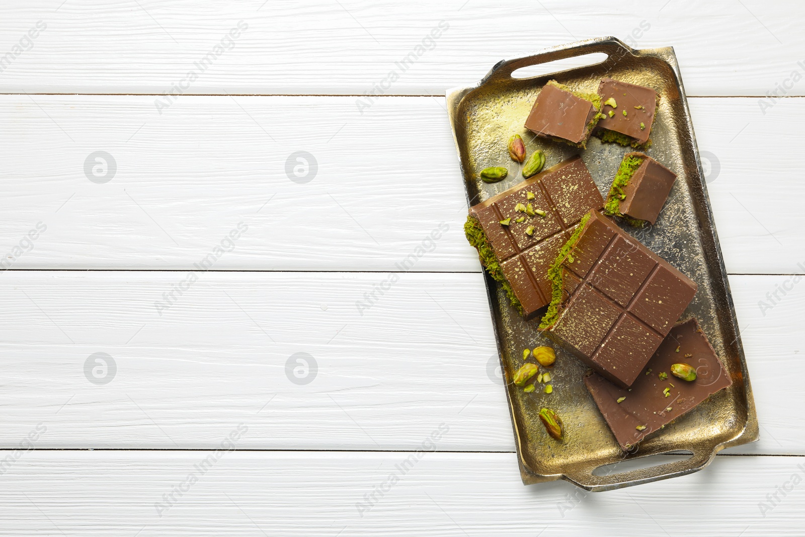 Photo of Pieces of Dubai chocolate bars with pistachios and knafeh on white wooden table, top view. Space for text